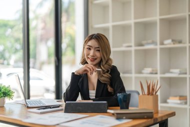 Ofis masasında oturmuş gülümseyen ve kameraya bakan Asyalı bir kadının portresi..