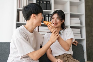 Genç çiftler tatillerini oturma odasında geçirirler. Genç adam rahat kıyafetler giyiyordu, yüzünü gösteriyordu, atıştırmalıkların tadından memnundu. Kanepede kruvasan yemek..