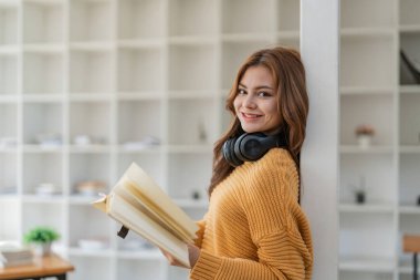 Genç Asyalı kadın evinde oturmuş kitap okuyor..