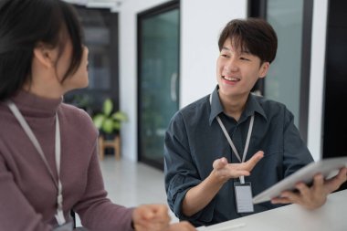 Tablete bakan iki Asyalı iş adamı takım çalışması stratejisini tartışıyor, ofiste bilgisayar laptopu üzerinde çalışıyor..