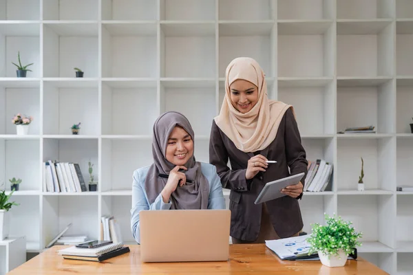 Two Business asian muslim women using laptop and tablet for working together in office, respect and collaboration concept.