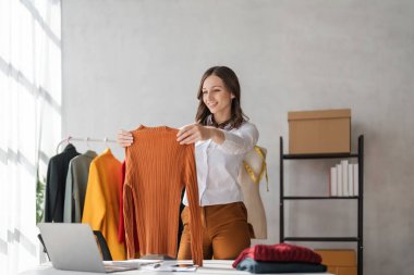 Terzi kadının portresi terzi atölyesinde giysiler üzerinde çalışıyor. Çekici genç bayan moda tasarımcısı gülümsemesi atölyede yeni el yapımı takım elbise yapma başarısı.