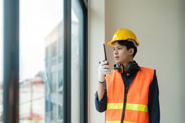 Asyalı erkek mühendis inşaat alanında duruyor ve telsizle iletişim kuruyor..