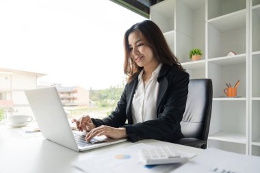 Ofisteki raporları incelerken bilgisayarını kullanan Asyalı iş kadını.