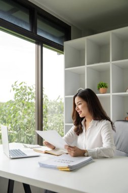 Ofisteki raporları incelerken bilgisayarını kullanan Asyalı iş kadını.