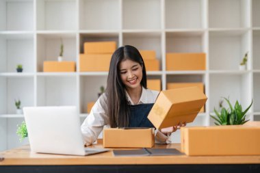 Küçük işletme girişimcisi KME, Asyalı mal sahibi, çevrimiçi sipariş veren bir müşteriye teslim edilmeye hazır bir paket tutuyor, ekommerce kavramı.