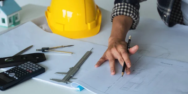 Closeup hand of engineer with construction work plan discussion together blueprint on working table in construction site with safety helmet.