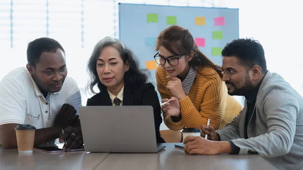 Happy senior old korean businesswoman discussing statistics concept on laptop with african american indian and asian male colleague working together workplace, analyzing electronic documents.