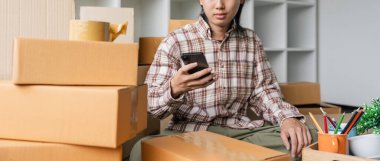 Genç adam taşınıyor. Yeni Evde Akıllı Telefon kullanan Asyalı Yetişkin Erkek Kutu ile çevrili.