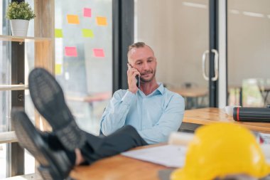 Kafkasyalı mühendis masaya bacak koyuyor ve ofisteki müşterilerle cep telefonuyla konuşuyor..