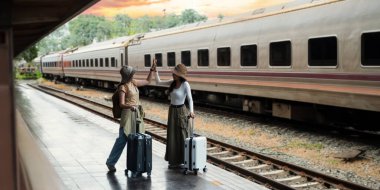 İki genç kadın, bavullarıyla mutlu bir şekilde tren turisti tatili bekliyor. Arka plan konsepti olarak seyahat ediyorlar. Aktif yaşam tarzı yolculukları ve seyahat yaşam tarzı.