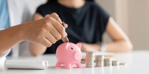 Family savings. Happy couple asian putting coin in piggybank while sitting together on desk at home, loving spouse planning budget and saving money for future.