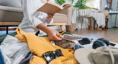 Making check list of thing to pack for travel. Woman writing paper take note and packing suitcase to vacation sitting on room, prepare clothes into luggage, Travel vacation travel. clipart