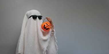 Komik Cadılar Bayramı Çocuğu kavramı, beyaz kostümlü şirin çocuk cadılar bayramı hayaleti elinde turuncu kabak hayaleti tutuyor..