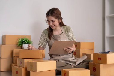 Asyalı kadın, onlara göndermeden önce kağıda bir müşteri listesi yazıyor. Web sitelerinde ve sosyal medyada ekomünikasyon işi yapıyor. Çevrimiçi ürün satma kavramı.