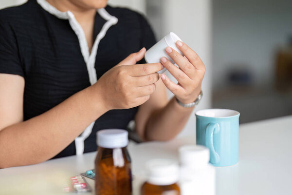 Woman hold bottle of drug tablet painkiller or vitamin supplement reading label ready to organizing medicine at home. medication healthcare concept.