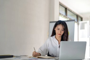 Güzel genç iş kadını Asyalı 'nın portresi ofis modern çalışma istasyonunda oturuyor ve dizüstü bilgisayarında yazıyor..