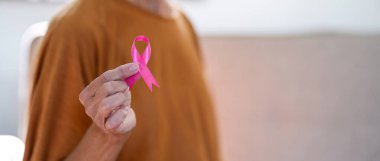 Evinde pembe kurdeleli kendinden emin, gülümseyen yaşlı bir kadının portresi. Sağlık, destek, önleme. Göğüs kanseri farkındalığı ayı konsepti.