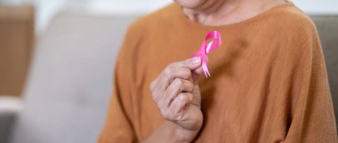 Evinde pembe kurdeleli kendinden emin, gülümseyen yaşlı bir kadının portresi. Sağlık, destek, önleme. Göğüs kanseri farkındalığı ayı konsepti.