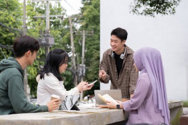 Çok ırklı sınıf arkadaşlarıyla birlikte kampüs parkında oturan öğrenci arkadaşlığı kavramı. Milenyum insanları dışarıda eğleniyor. Gençlik ve eğitim.