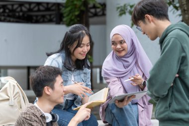 Çok ırklı sınıf arkadaşlarıyla birlikte kampüs parkında oturan öğrenci arkadaşlığı kavramı. Milenyum insanları dışarıda eğleniyor. Gençlik ve eğitim.