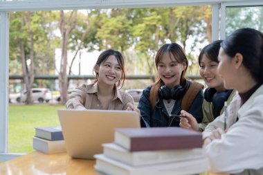 Üniversite öğrencileri kitap ve dizüstü bilgisayarlarla aynı masada oturuyorlar. Üniversite kampüsünde grup çalışması yapan mutlu gençler..