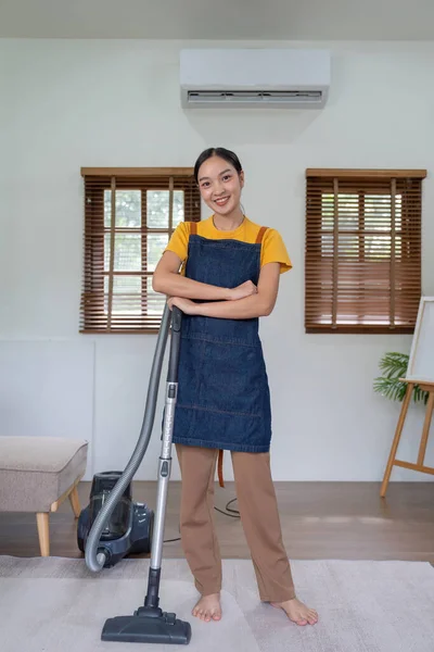 Asian lady doing house chores in apron. young housewife using vacuum clean the floor in the living room.
