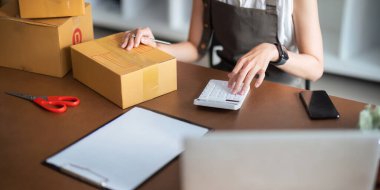 Serbest çalışan Asyalı kadın girişimci online sipariş almak ve gözden geçirmek için dizüstü bilgisayar ve hesap makinesi kullanıyor. Müşterilere, çevrimiçi küçük işletme fikirlerine satış hazırlamak için..