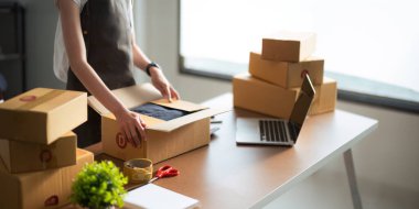 Genç kadın satıcıyı kapatın ve müşteriye teslim etmek için bir paket ürün hazırlayın. Çevrimiçi satış, ekommerce. Genç bir kadın çevrimiçi ecommerce alışverişinde çalışıyor..