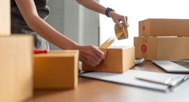 Asyalı kadın, paketleme, nakliye, çevrimiçi satış İnternet pazarlama ekommerce konsepti başlangıç iş fikri için paket kutuları eklemek için koli bandı kullanıyor.