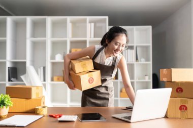 Girişim KOBİ küçük işletme girişimcisi. İnternetten sipariş almak ve gözden geçirmek için dizüstü bilgisayar ve kutu kullanan serbest Asyalı kadın müşterilere, çevrimiçi iş fikirlerine satış hazırlamak için internetten sipariş alıyor ve gözden geçiriyor..