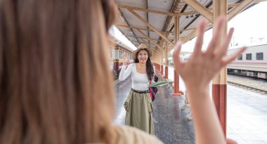 Asyalı bayan turist dalgaları tren istasyonunda bir yolculuğa çıkan arkadaşa merhaba diyor..