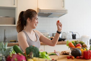 Genç Asyalı sağlıklı, günlük kıyafetlerle güzel bir kadın gülümsemek ve domates doğramak. Tatilde evde diyet yapmak için evde meyve yemek..