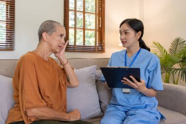 Asyalı genç kadın bakıcı doktor ev ziyareti sırasında yaşlı kadın hastalara danışma ve yazma sorunu veriyor.