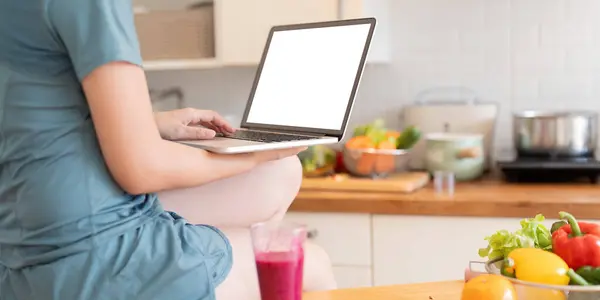 Woman using personal laptop with blank empty screen with copy space, typing on keyboard, looking for new healthy recipes online, mock up.