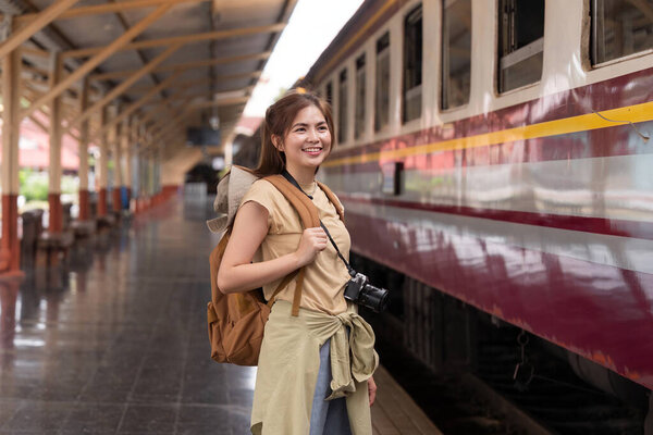 Beautiful asian traveler with backpack getting on a train at a platform of railway station.
