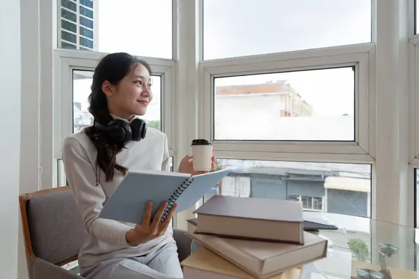 Young beautiful woman asian holding coffee and read a book while relax during work at home.