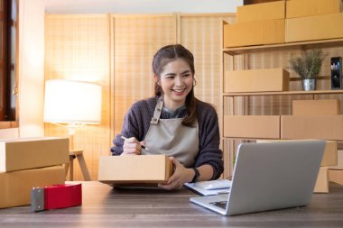 Asyalı kadın, onlara göndermeden önce kağıda bir müşteri listesi yazıyor. Web sitelerinde ve sosyal medyada ekomünikasyon işi yapıyor. Çevrimiçi ürün satma kavramı.