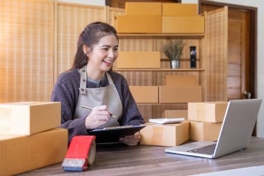 İnternetten ecommerce alışverişinde çalışan genç bir kadın. Genç kadın satıcı müşteriye teslim etmek için bir paket ürün hazırla. Çevrimiçi satış, ekommerce. Ürün çevrimiçi satılıyor.