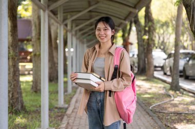 Sırt çantası ve kitabı olan güzel bir Asyalı kadın. Üniversite öğrencisi kampüste bir sürü kitap taşıyor..