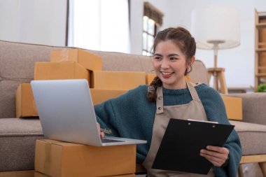 İnternetten ecommerce alışverişinde çalışan genç bir kadın. Genç kadın satıcı müşteriye teslim etmek için bir paket ürün hazırla. Çevrimiçi satış, ekommerce. Ürün çevrimiçi satılıyor.