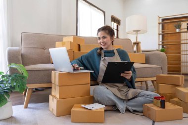 İnternetten ecommerce alışverişinde çalışan genç bir kadın. Genç kadın satıcı müşteriye teslim etmek için bir paket ürün hazırla. Çevrimiçi satış, ekommerce. Ürün çevrimiçi satılıyor.