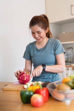 Evdeki mutfakta meyve ve sebze doğrayan Asyalı kadın smoothie hazırlıyor..