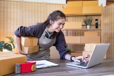 İnternetten ecommerce alışverişinde çalışan genç bir kadın. Genç kadın satıcı müşteriye teslim etmek için bir paket ürün hazırla. Çevrimiçi satış, ekommerce. Ürün çevrimiçi satılıyor.