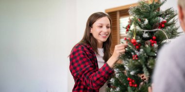 Mutlu son sınıf kadını ve yetişkin kızı Noel ağacını evde süslüyor..