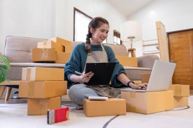 İnternetten ecommerce alışverişinde çalışan genç bir kadın. Genç kadın satıcı müşteriye teslim etmek için bir paket ürün hazırla. Çevrimiçi satış, ekommerce. Ürün çevrimiçi satılıyor.