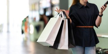 Akıllı telefon kullanan bir kadın alışveriş merkezinin yanında dururken Kara Cuma alışveriş çantası tutuyor..