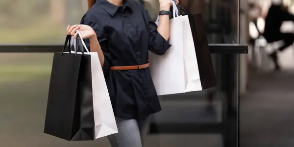 Close up of woman hand holding shopping bag while walking near mall on holidays Black Friday.