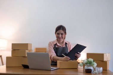 Kadın, onlara göndermeden önce kutuya bir müşteri listesi yazıyor. Web sitelerinde ve sosyal medyada ekomünikasyon işi yürütüyor. Çevrimiçi ürün satma kavramı.