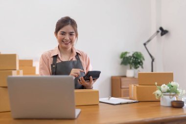 İnternetten ecommerce alışverişinde çalışan genç bir kadın. Genç bir kadın müşteriye teslim etmek için bir paket ürün satar. Çevrimiçi satış, ekommerce. Ürün çevrimiçi satılıyor.